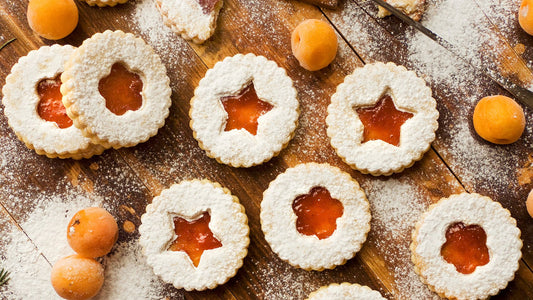 Veganské vánoční linecké cukroví ve tvaru hvězdiček, posypané moučkovým cukrem a plněné malinovou marmeládou, podávané na rustikálním vánočním pozadí.