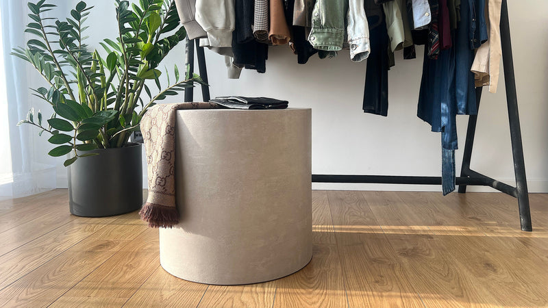 Noční stolek z mikrobetonu v moderním interiéru, doplněný rostlinou a oblečením. Minimalistický design ideální pro stylové a praktické využití v domácnosti.