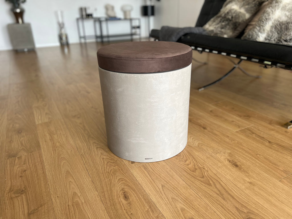 Mikrobetonový taburet se sedákem v hnědé barvě, umístěný na dřevěné podlaze v moderním obývacím pokoji.