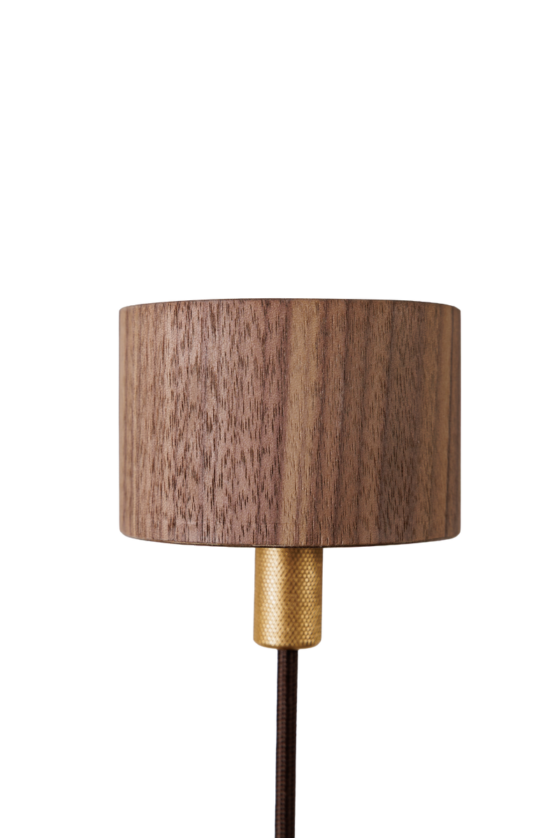 Detailní záběr na moderní dřevěnou stolní lampu s cylindrickým stínidlem z ořechového dřeva a zlatou kovovou základnou, umístěnou na transparentním pozadí pro jasnou viditelnost detailů produktu.