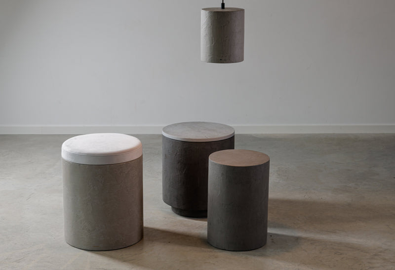 Sada kulatých mikrobetonových stolků a taburetů v šedých odstínech s látkovým sedákem a závěsným betonovým svítidlem, moderní minimalistický interiérový design