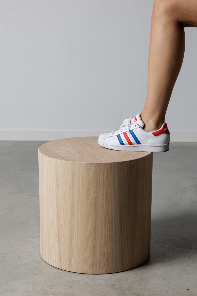 Noční stolek z dřevěného mikrobetonu s jednoduchým designem, na kterém je postavena noha v teniskách. Moderní a funkční doplněk pro každý interiér.