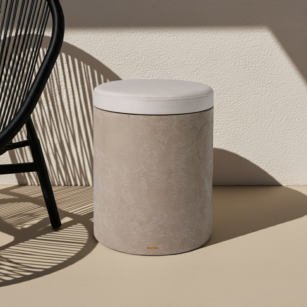Světle béžový mikrobetonový odkládací stolek s kulatým bílým podsedákem, stojící na béžové podlaze se stínem vedle tmavé designové židle, ideální jako stylová taburetka nebo noční stolek.